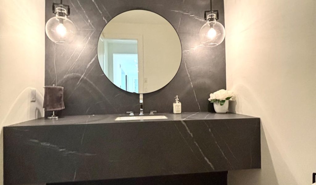 Grey slate looking counter and back feature wall, with a round mirror and two wall sconces